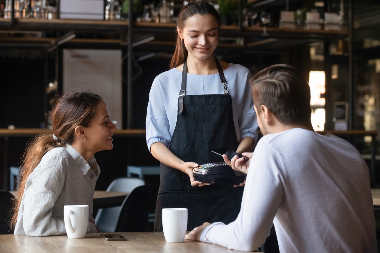 Smiling cafe customer paying with a contactless card at the counter